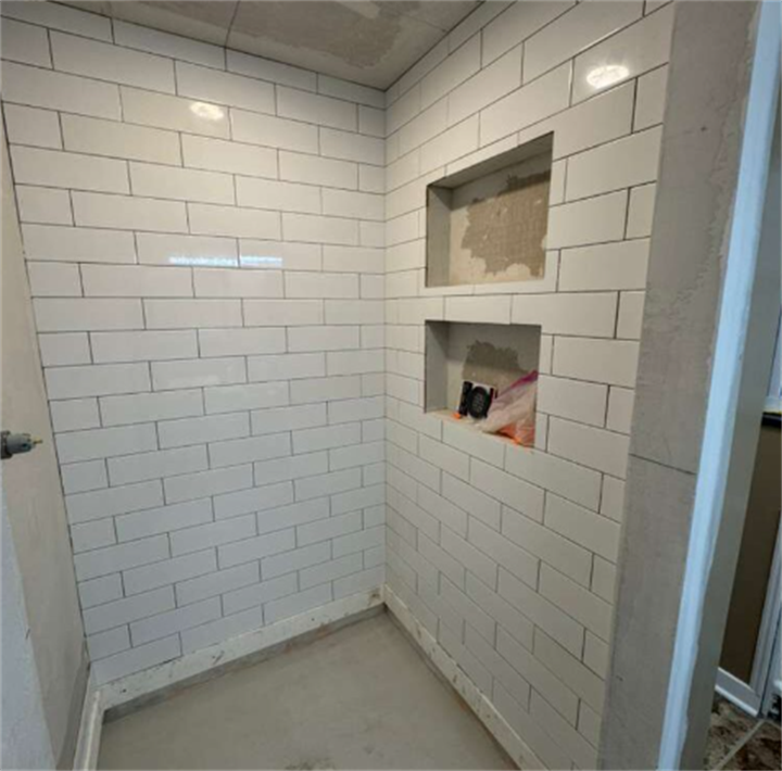 Unfinished shower space with white subway tile and recessed niches during bathroom renovation