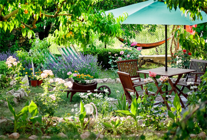 Shaded backyard oasis featuring wooden patio table, dense flowering gardens, shade trees and outdoor lounge space
