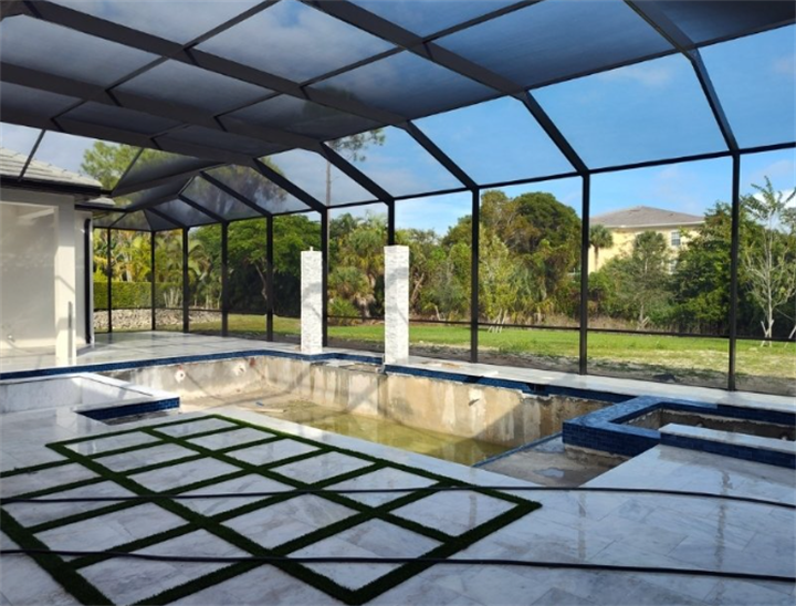 Newly constructed black screen pool enclosure surrounding unfinished swimming pool with marble tiled patio