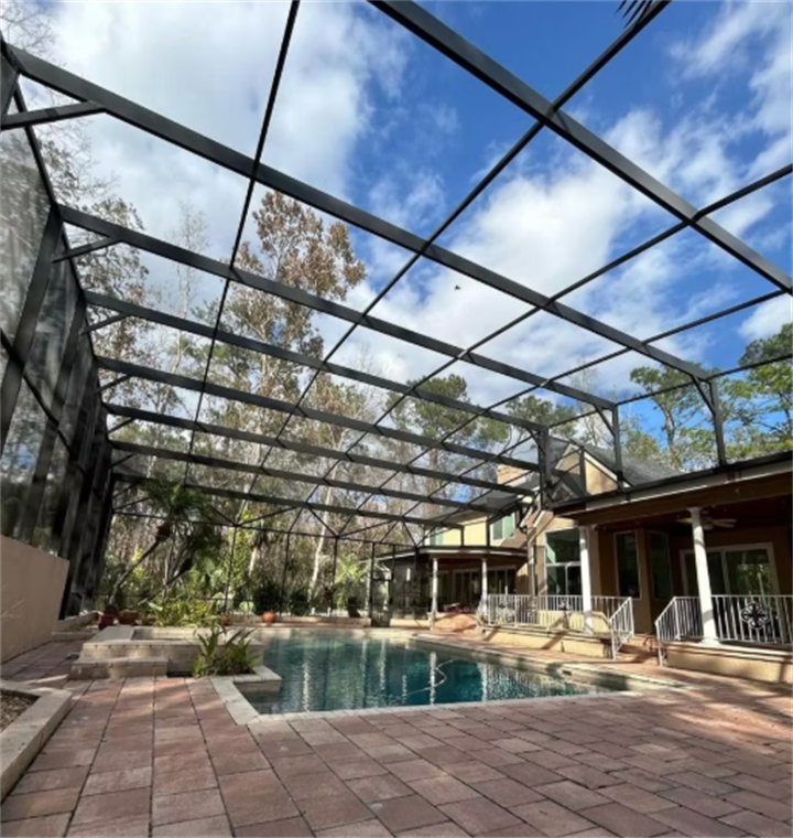 Large black aluminum pool screen enclosure over brick paver patio and residential swimming pool, Florida backyard