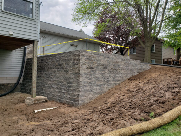 Minnesota residential segmented block retaining wall under construction with sloped backyard soil