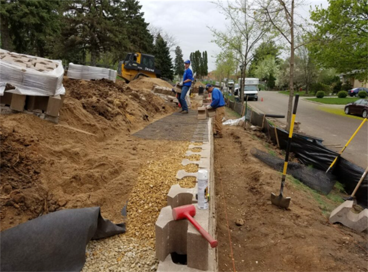 Workers laying gravel foundation for retaining wall installation in Minnesota residential excavation site
