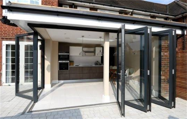 Wide open black framed bifold doors connecting home kitchen to paved backyard patio