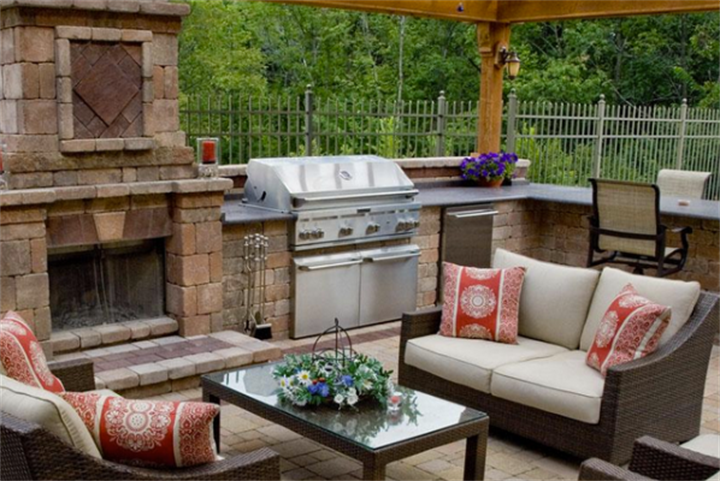 Stone outdoor kitchen with built-in grill and fireplace leveled on sloped garden terrace